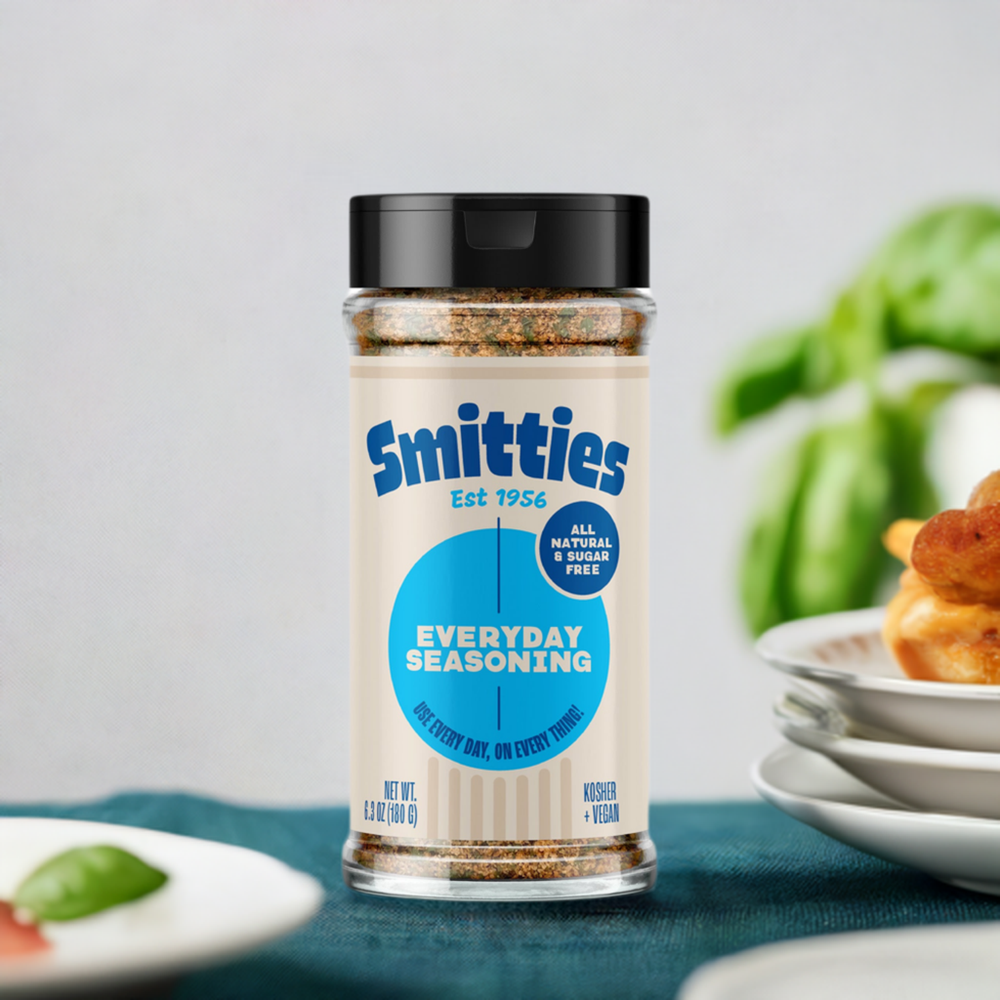 A shaker of Smitties Everyday seasoning on a teal tablecloth, with several plates in the background.