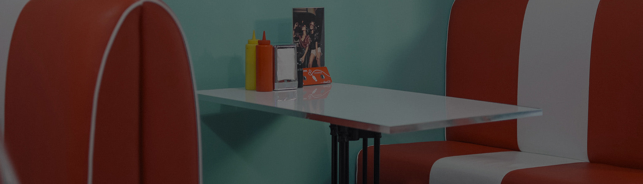 A muted picture of a 60s-style diner booth, with bottles of ketchup and mustard, a napkin dispenser, and a photograph on the table.