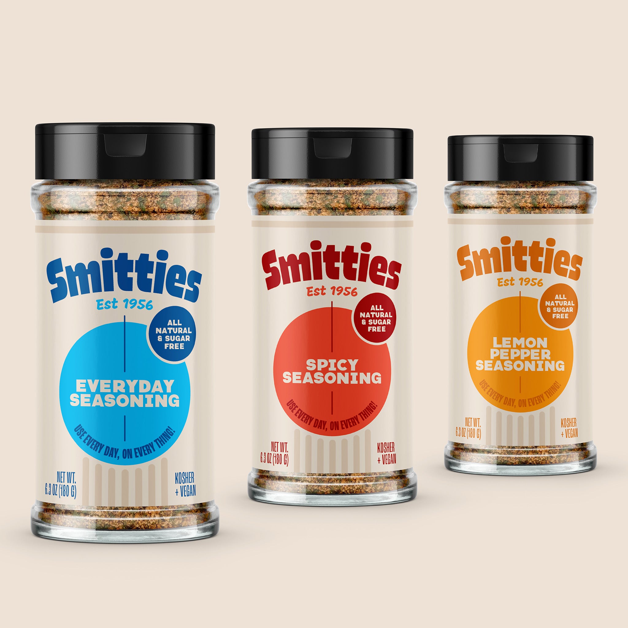 Shakers of Smitties brand seasonings on an off-white background. From left to right: Smitties Everyday Seasoning, Smitties Spicy Seasoning, and Smitties Lemon Pepper Seasoning. Shakers get further from the foreground from left to right.