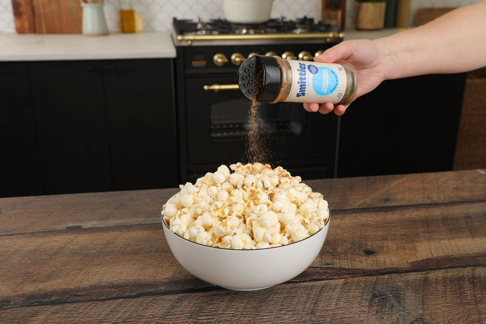 A hand shaking Smitties Everyday Seasoning over a bowl of popcorn.